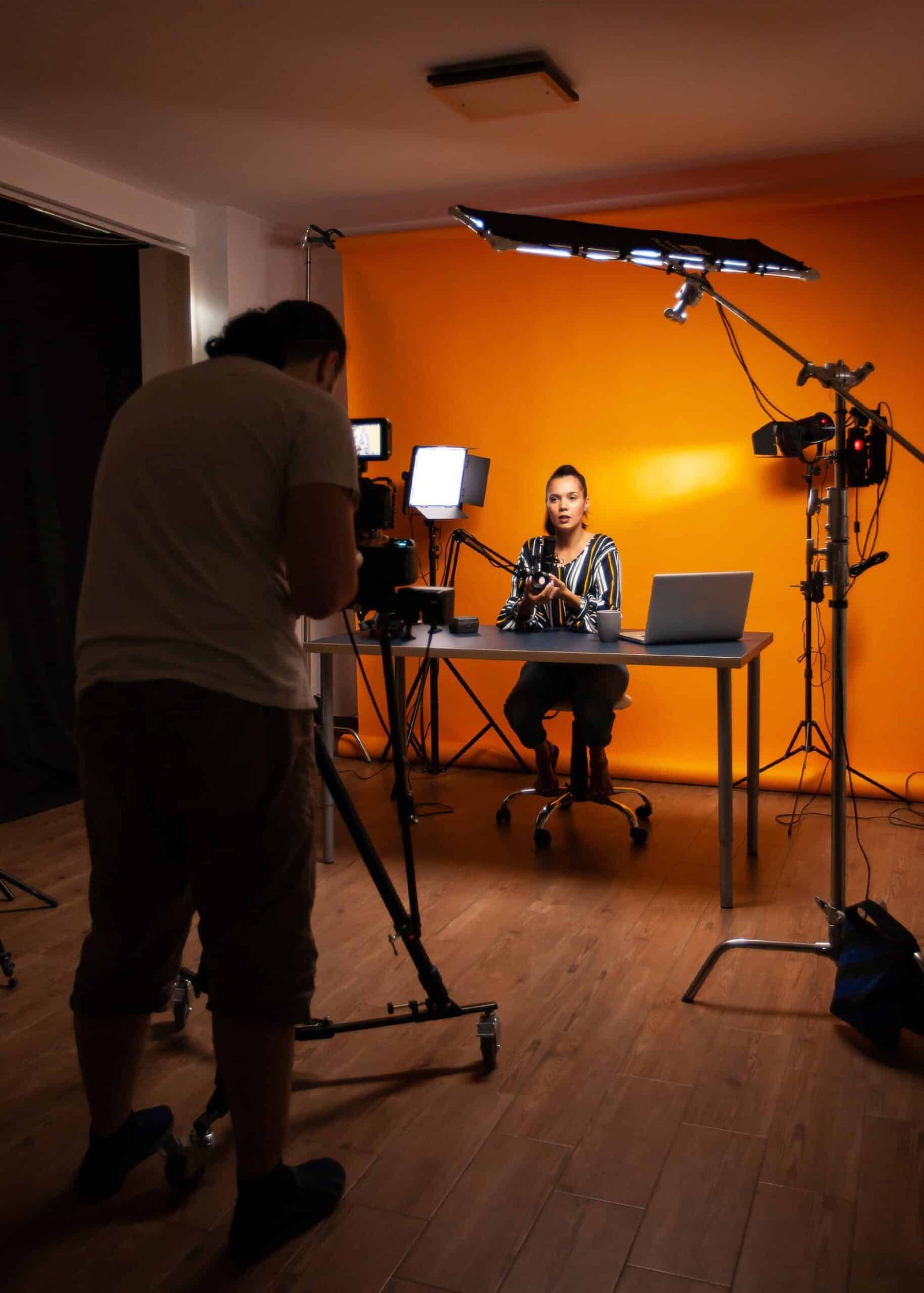 A photography instructor was filmed in a studio setup with lights, a camera, and a laptop for an online training session.